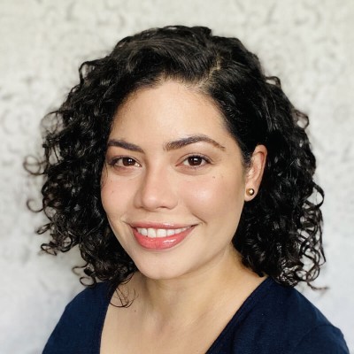 A smiling Latina woman with curly dark hair to her shoulders and wearing a black top
