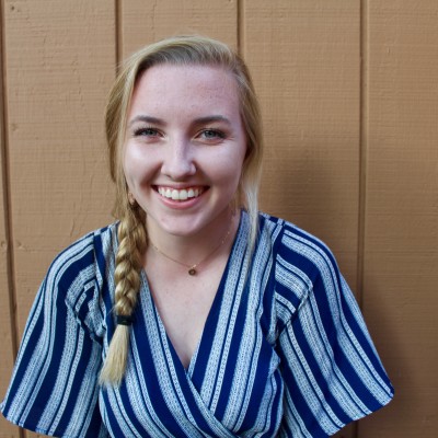 A white with a long blonde braid over one shoulder smiles while wearing a blue-striped shirt
